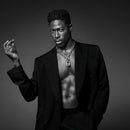 Man wearing a black suit with a chain necklace against a dark background