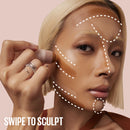 Person applying makeup with a brush, focusing on facial features, on a pink background.