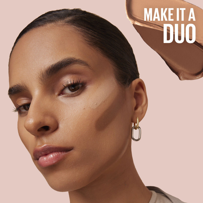 Close-up of a woman's face with a makeup product labeled 'MAKE IT A DUO' on a pink background.