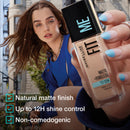 Woman holding a Maybelline Fit Me foundation bottle with product features displayed.