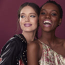 Two women standing close together against a pink background