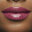 Close-up of a person's lips wearing a glossy purple lipstick on a matching skin tone.