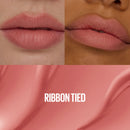 Close-up of lips with a swatch of 'Ribbon Tied' color on a pink background