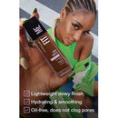 Woman holding a bottle of foundation with product details on a blurred street background