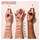 Three hands holding lip glosses with swatches on wrists against a light pink background.