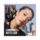 Woman wearing earrings with a cityscape background and text 'Luminous Matte Look'.