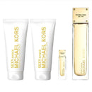 Michael Kors Sexy Amber gift set featuring two white body care tubes with gold lettering, a small matching sample vial, and a tall rectangular perfume bottle with a gold cap on a white background.