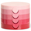 A stack of four round cosmetic containers in a vertical gradient from pale pink to coral red, with a matching pink sliding lid on the front, photographed on a white background.