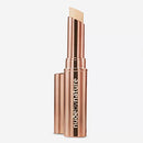 Bronze-colored concealer stick with 'Nude by Nature' branding on a white background