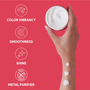 A hand holding an open white cosmetic jar against a coral-pink background, with four white text icons on the left reading Color Vibrancy, Smoothness, Shine, and Metal Purifier. Three dollops of white cream are shown on the wrist.