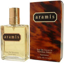 A bottle of Aramis Eau de Toilette Natural Spray with its packaging box. The bottle is clear and gold-colored, and the box has a marbled brown and gold design with the Aramis logo.